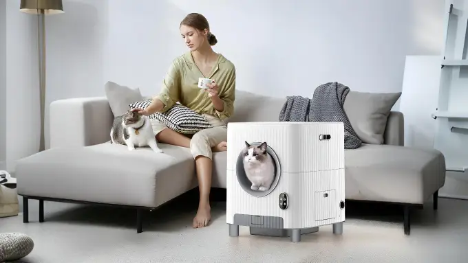 Woman relaxing on a sofa with two cats, one inside a smart litter box.