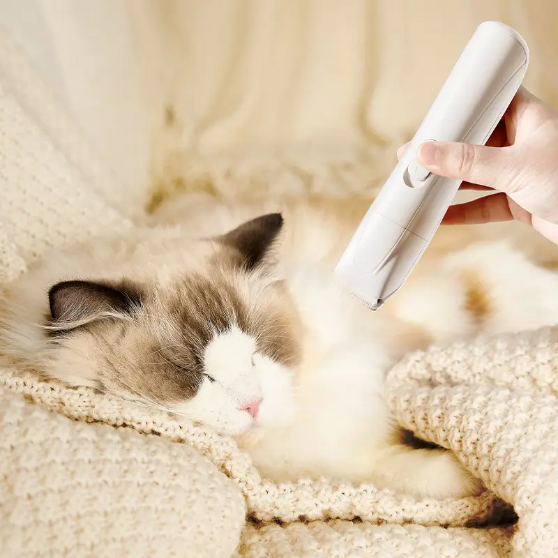 Pet clipper being used to groom a relaxed, fluffy cat on a cozy blanket.
